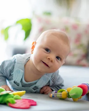 Bebé sonriendo mientras está boca abajo, rodeado de juguetes suaves y coloridos en una habitación acogedora.