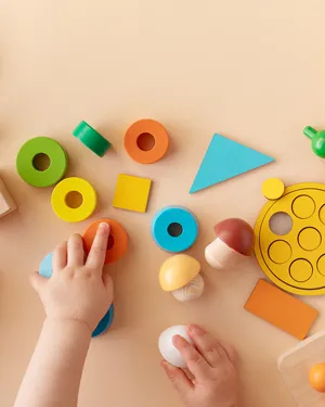 Manitas de bebé jugando con bloques educativos de madera y figuras geométricas de colores sobre una superficie beige.