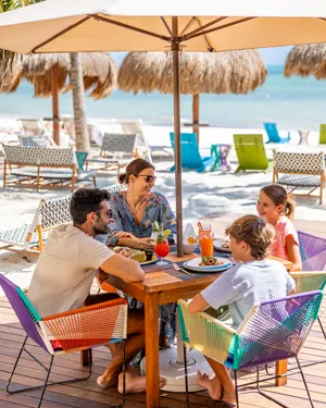 Una familia comiendo en un restaurante junto a la playa bajo una sombrilla.